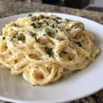 Close-up of fettuccine pasta coated in rich Olive Garden Alfredo Sauce, topped with Parmesan and parsley.