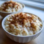 Close-up of creamy rice pudding in a white bowl, generously sprinkled with cinnamon.