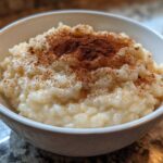 Close-up of creamy rice pudding in a white bowl, generously dusted with ground cinnamon.