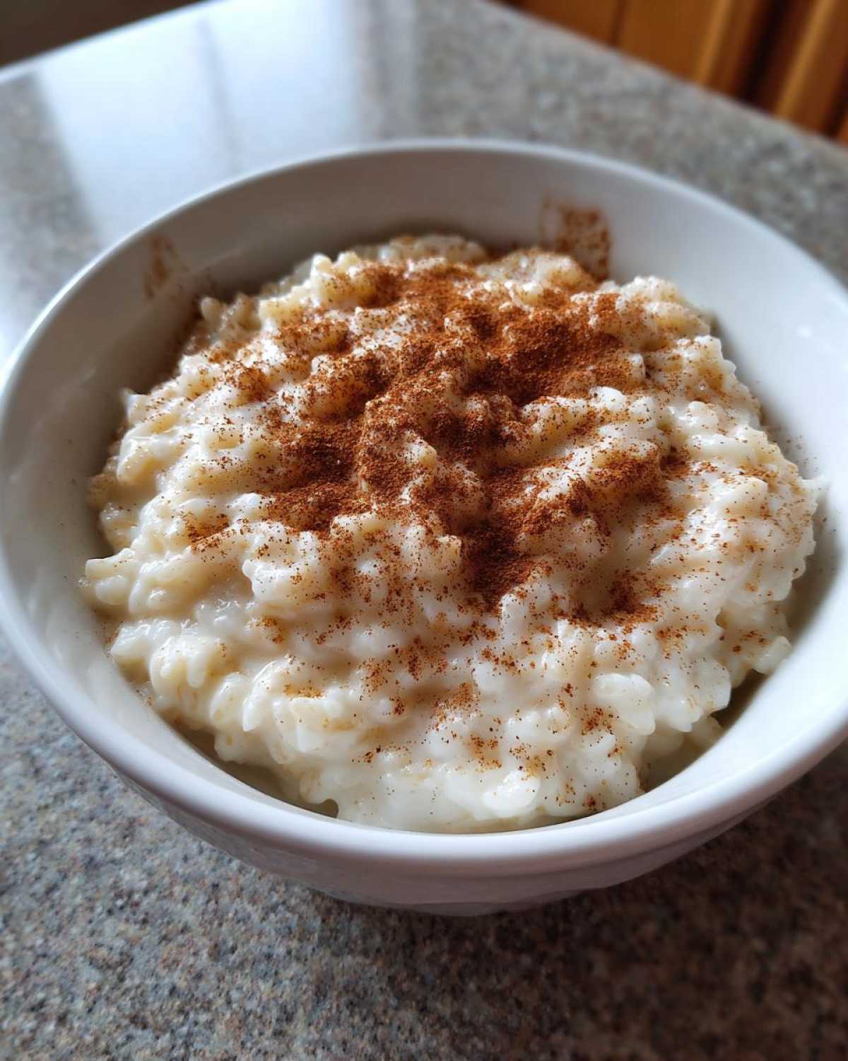 A close-up of creamy rice pudding served in a white bowl and generously dusted with ground cinnamon.