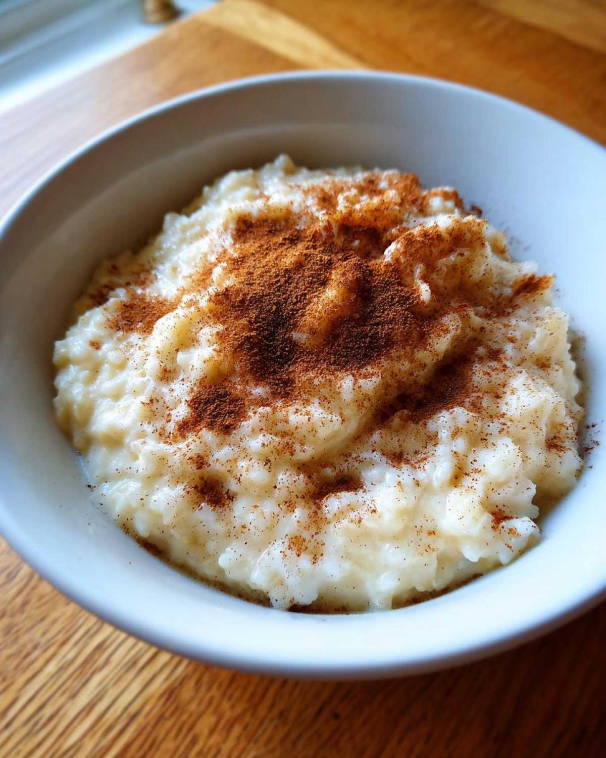 A close-up of creamy rice pudding served in a white bowl, generously dusted with cinnamon.