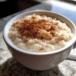 Close-up of creamy rice pudding recipe served in a white mug, generously sprinkled with cinnamon.