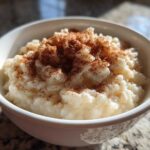 A close-up of a white bowl filled with creamy rice pudding recipe, generously dusted with cinnamon.
