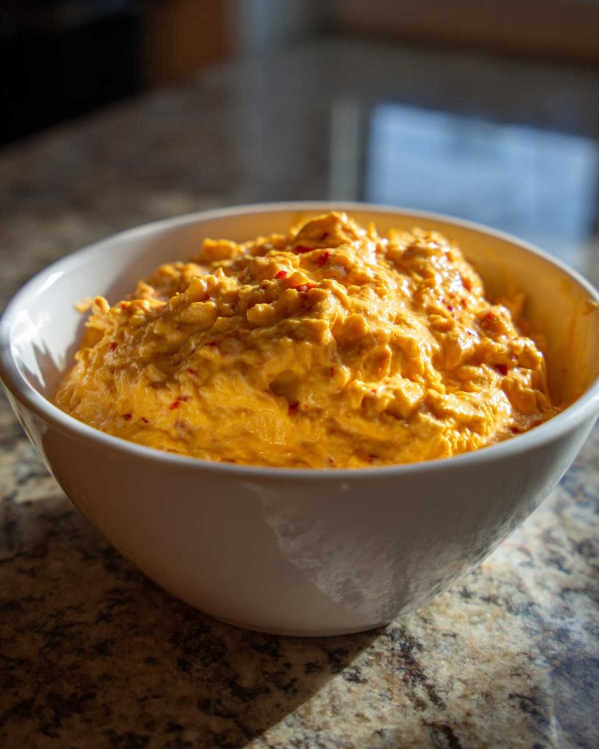 A close-up of thick, creamy, orange rotel dip served in a white bowl on a speckled countertop.