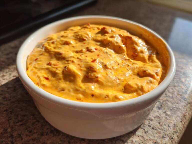 Close-up of hot, creamy orange Rotel dip served in a small white bowl on a granite countertop.