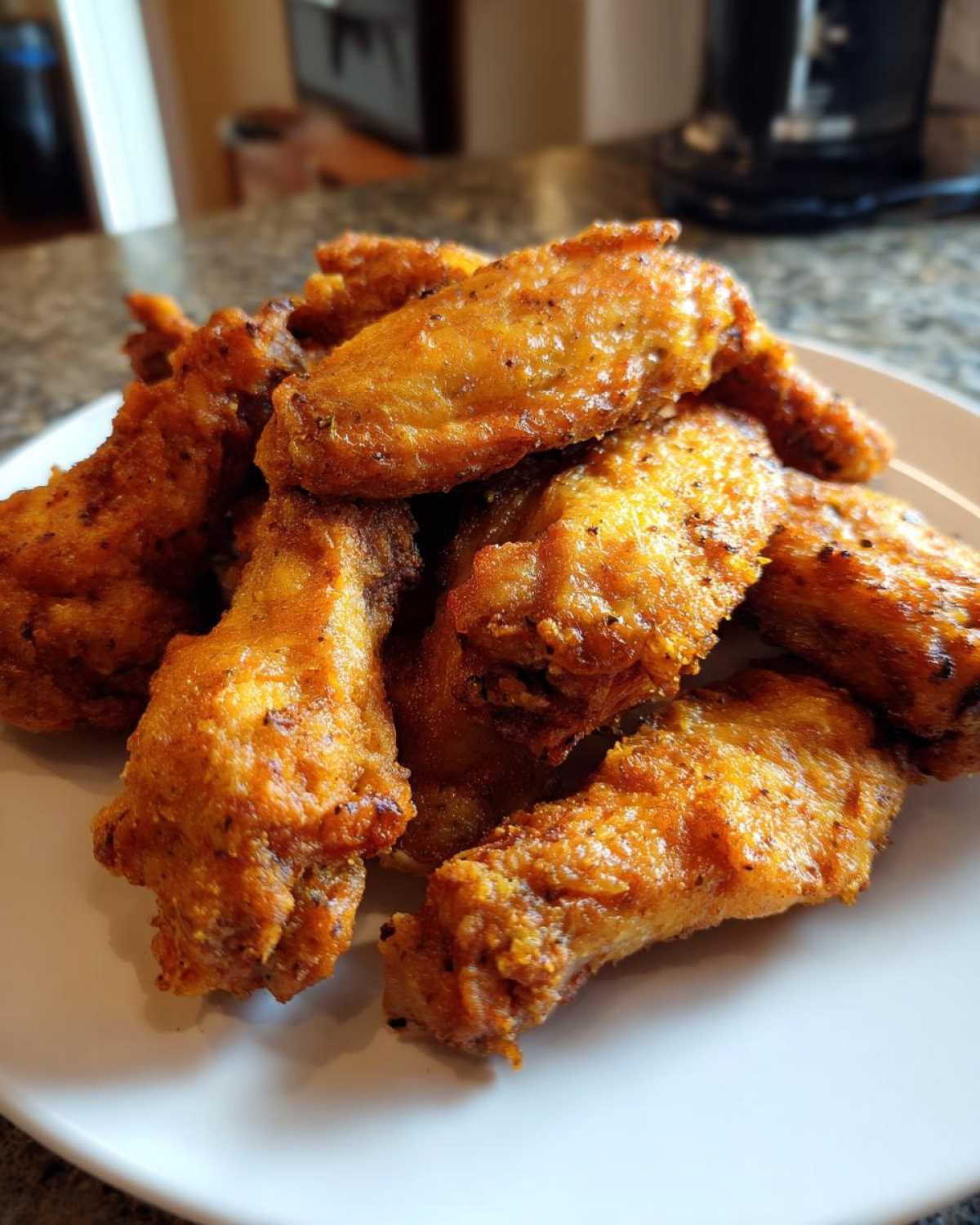 A close-up of a pile of golden brown, crispy air fryer chicken wings seasoned with pepper on a white plate.