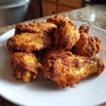 A pile of golden brown, seasoned, crispy air fryer chicken wings served on a white plate.