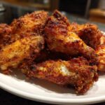 A close-up of several golden brown, seasoned, crispy baked chicken wings piled on a white plate.