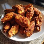 A pile of golden brown, perfectly coated crispy baked chicken wings served on a white plate.