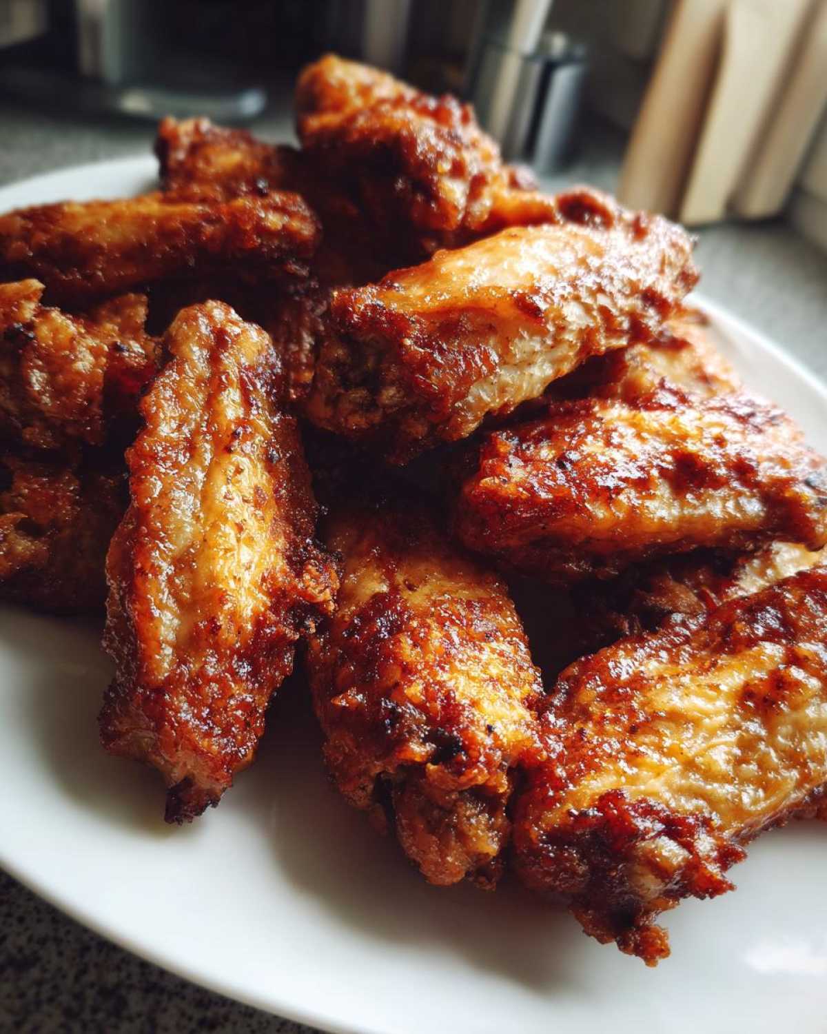 A close-up of several golden-brown, perfectly crispy baked chicken wings piled on a white plate.