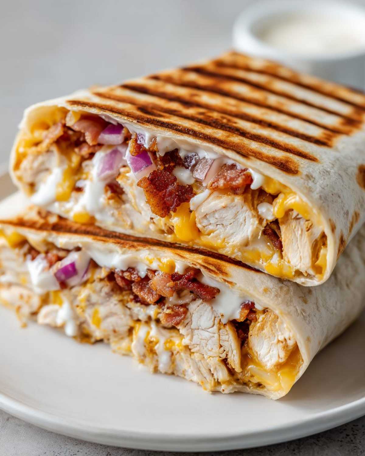 A grilled chicken bacon ranch wrap cut in half, showing layers of chicken, bacon, cheese, and ranch dressing.