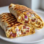 Cross-section view of a grilled chicken bacon ranch wrap, showing creamy ranch sauce, chicken, bacon, and red onion.