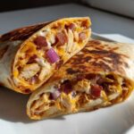 A crispy chicken bacon ranch wrap cut in half, showing shredded chicken, bacon, cheese, and ranch dressing.