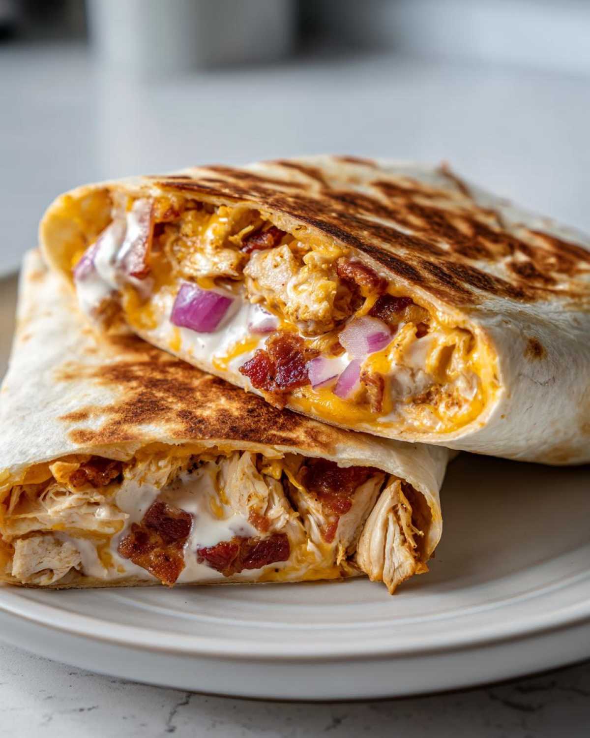 Two halves of a crispy chicken bacon ranch wrap stacked, showing shredded chicken, bacon, cheese, and ranch dressing.