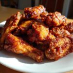 A pile of perfectly crispy, glazed chicken wing pieces served on a white plate under bright light.