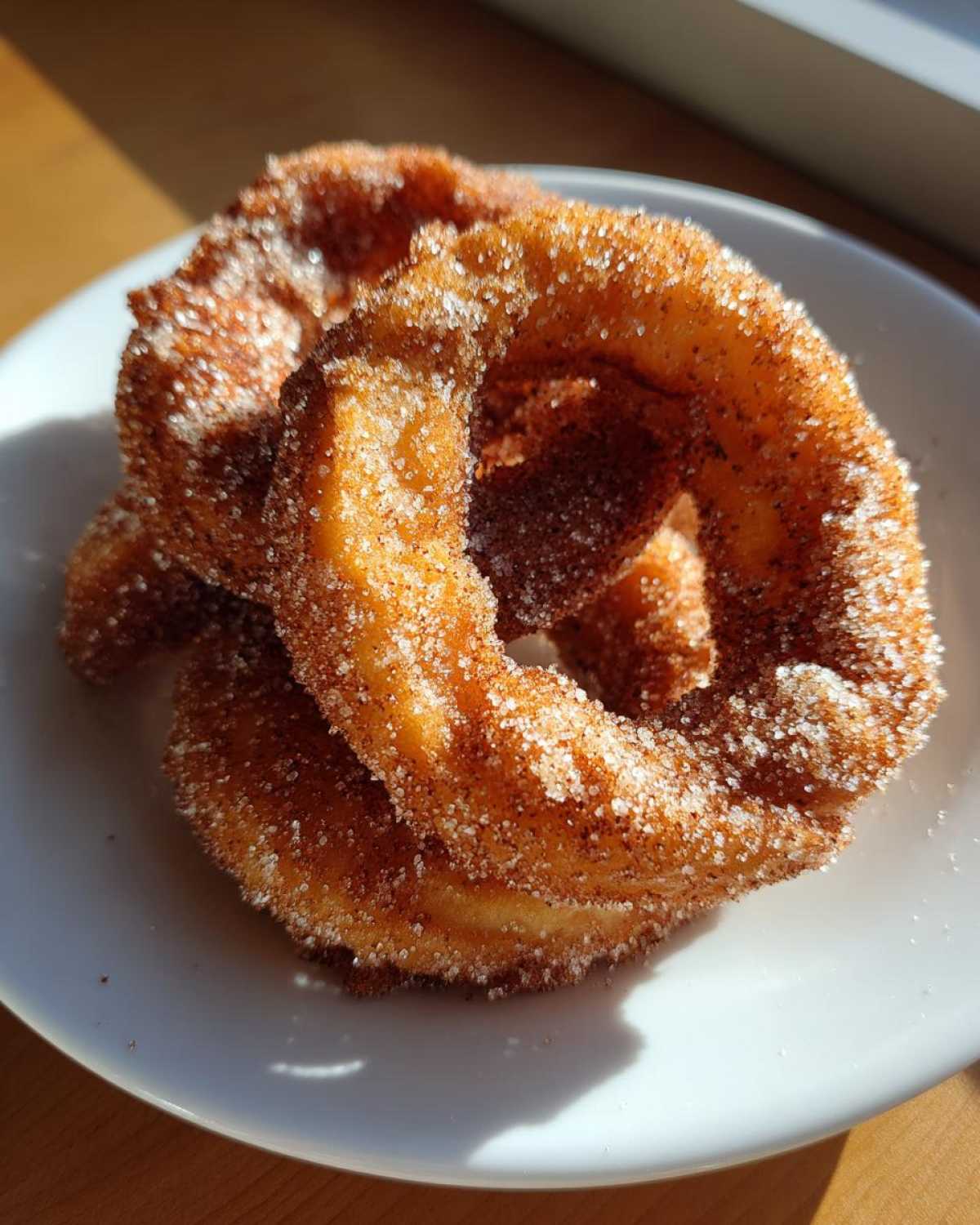 Close-up of two crispy, golden-brown buñuelos heavily coated in cinnamon sugar, resting on a white plate.