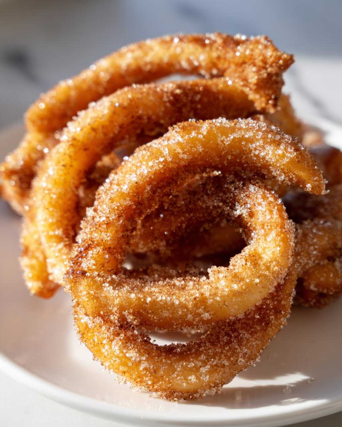 Close-up of several crispy, golden-brown buñuelos rings heavily coated in sparkling cinnamon sugar.