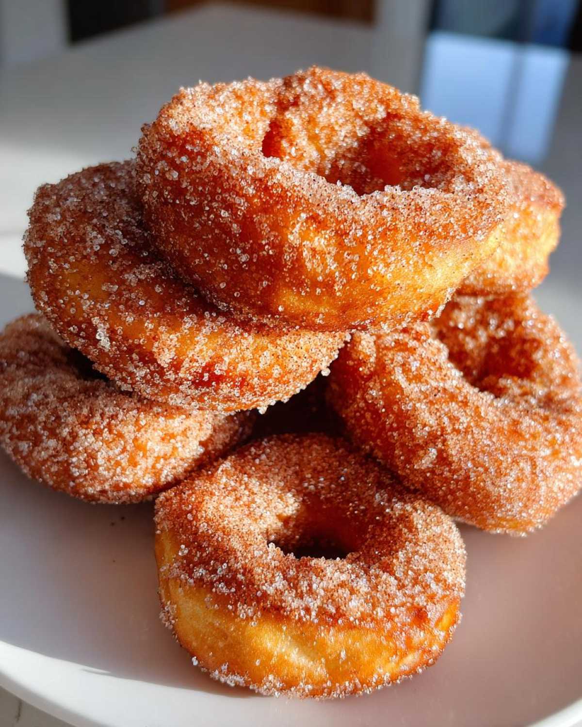 A close-up stack of golden brown, crispy buñuelos heavily coated in cinnamon sugar.