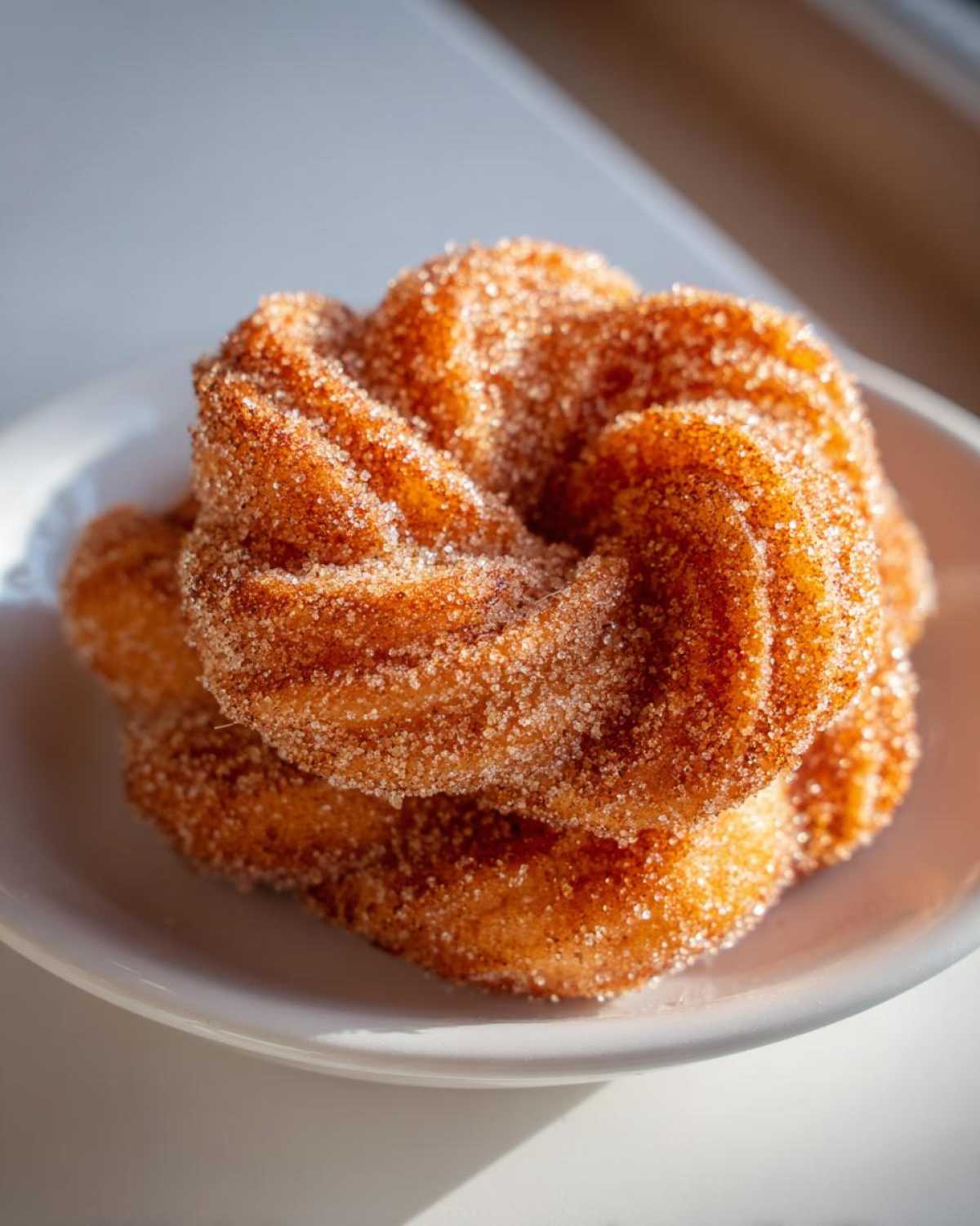 Close-up of two crispy, golden brown buñuelos generously coated in cinnamon sugar, resting on a white plate.