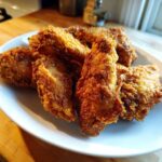 A close-up of several golden-brown, crispy fried chicken wings piled on a white plate.