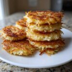 A stack of golden brown, crispy potato pancakes served on a white plate.