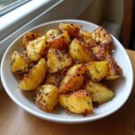 A white bowl filled with golden brown, crispy roast potatoes seasoned with herbs.