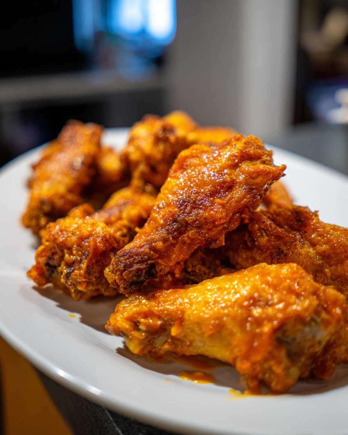 A close-up of several crispy, saucy chicken wings piled on a white plate.