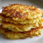 A close-up stack of four golden-brown, crispy potato pancakes on a white plate.