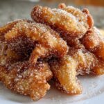 A close-up of a pile of golden brown, crispy buñuelos heavily coated in granulated sugar.