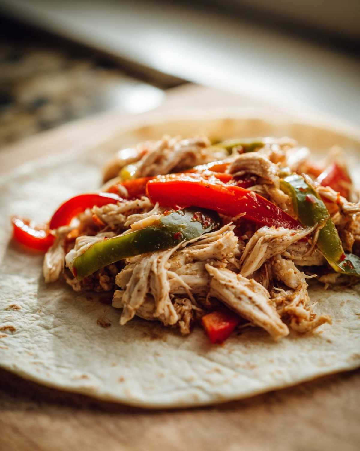Close-up of shredded chicken and colorful bell peppers ready to be rolled into a tortilla for crockpot chicken fajitas.