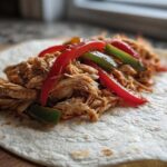 Shredded chicken filling with red and green peppers ready for crockpot chicken fajitas on a flour tortilla.