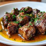 Close-up of tender, cubed crockpot steak bites glistening in a rich, savory sauce and topped with fresh parsley.