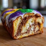 A close-up cross-section of a homemade king cake showing rich cinnamon swirl filling and Mardi Gras colored sprinkles.