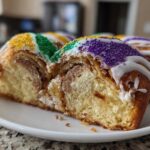 Close-up of a sliced king cake showing the cinnamon swirl interior and purple, green, and gold Mardi Gras sprinkles.