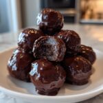 A stack of rich, dark chocolate coated Oreo balls, one with a bite taken out showing the dark center.