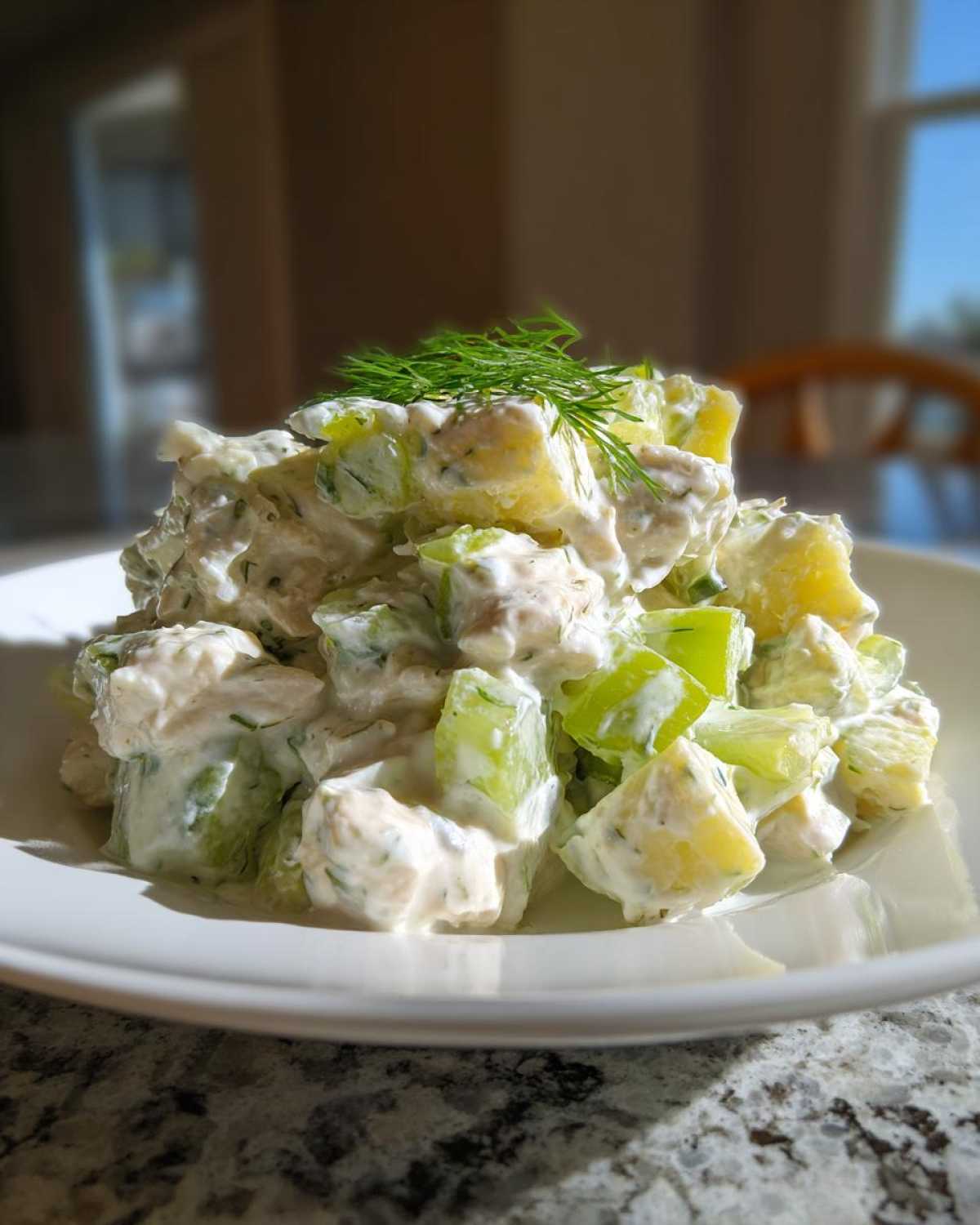 A mound of creamy dill pickle chicken salad featuring chunks of chicken, pickles, and topped with fresh dill sprigs.