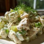 A close-up of a mound of creamy dill pickle chicken salad garnished with fresh dill.