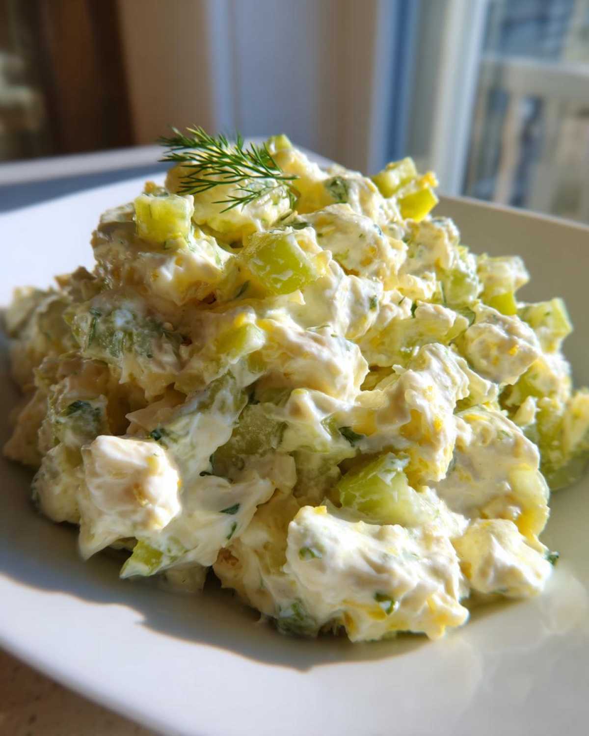A close-up of creamy dill pickle chicken salad piled high on a white plate, garnished with a sprig of fresh dill.
