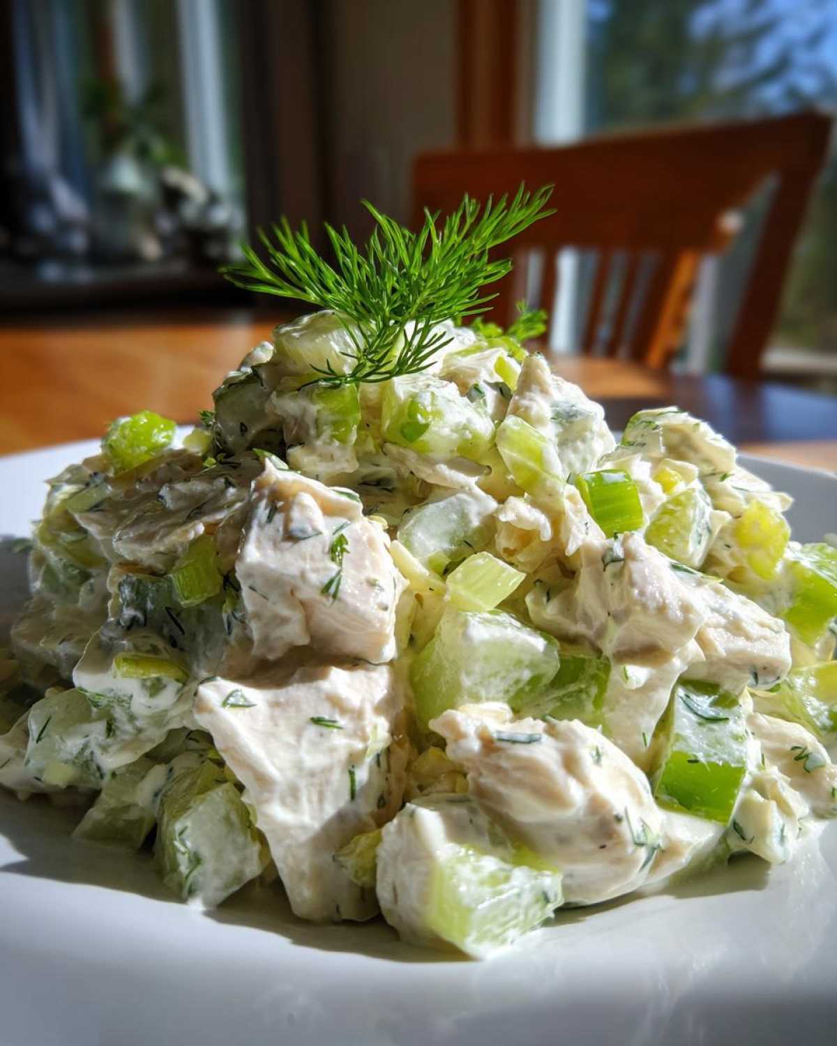 Close-up of a mound of creamy dill pickle chicken salad, featuring chunks of chicken and celery, topped with fresh dill.