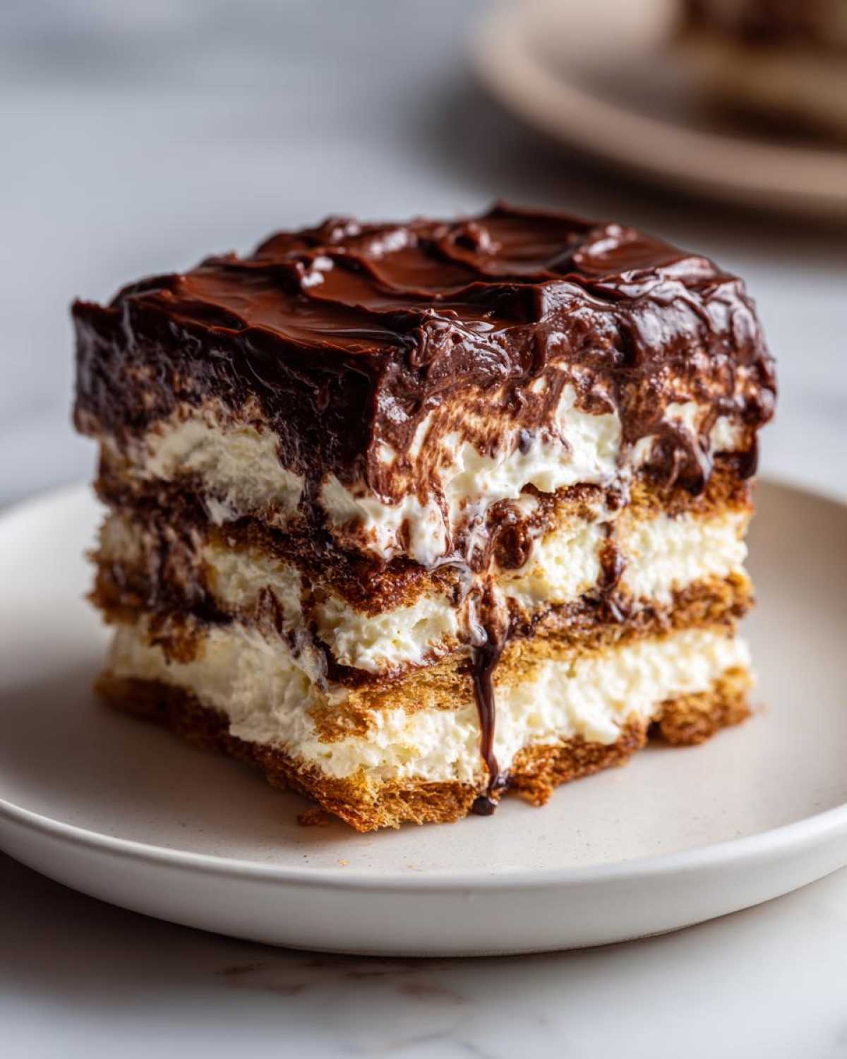 A decadent slice of eclair cake showing layers of graham crackers, cream filling, and thick chocolate frosting.