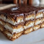 A thick slice of layered eclair cake featuring graham crackers, creamy filling, and rich chocolate ganache topping.