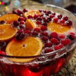 Close-up of a vibrant red champagne punch garnished with floating orange slices and whole cranberries.