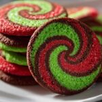 Close-up of colorful red, green, and chocolate pinwheel cookies stacked on a white plate.