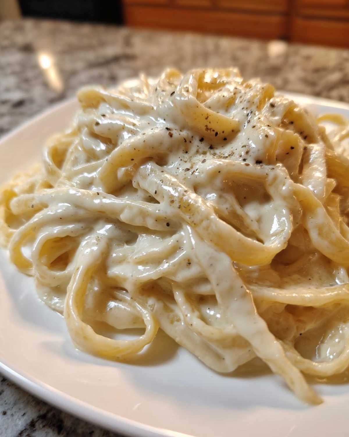 Close-up of fettuccine pasta generously coated in creamy homemade alfredo sauce and topped with black pepper.