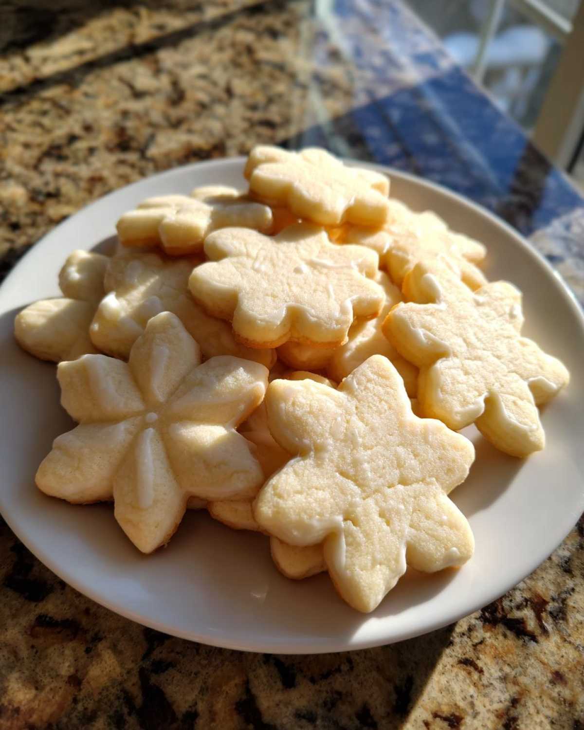 A pile of freshly baked, flower-shaped vegan sugar cookies with a thin white glaze on a white plate.