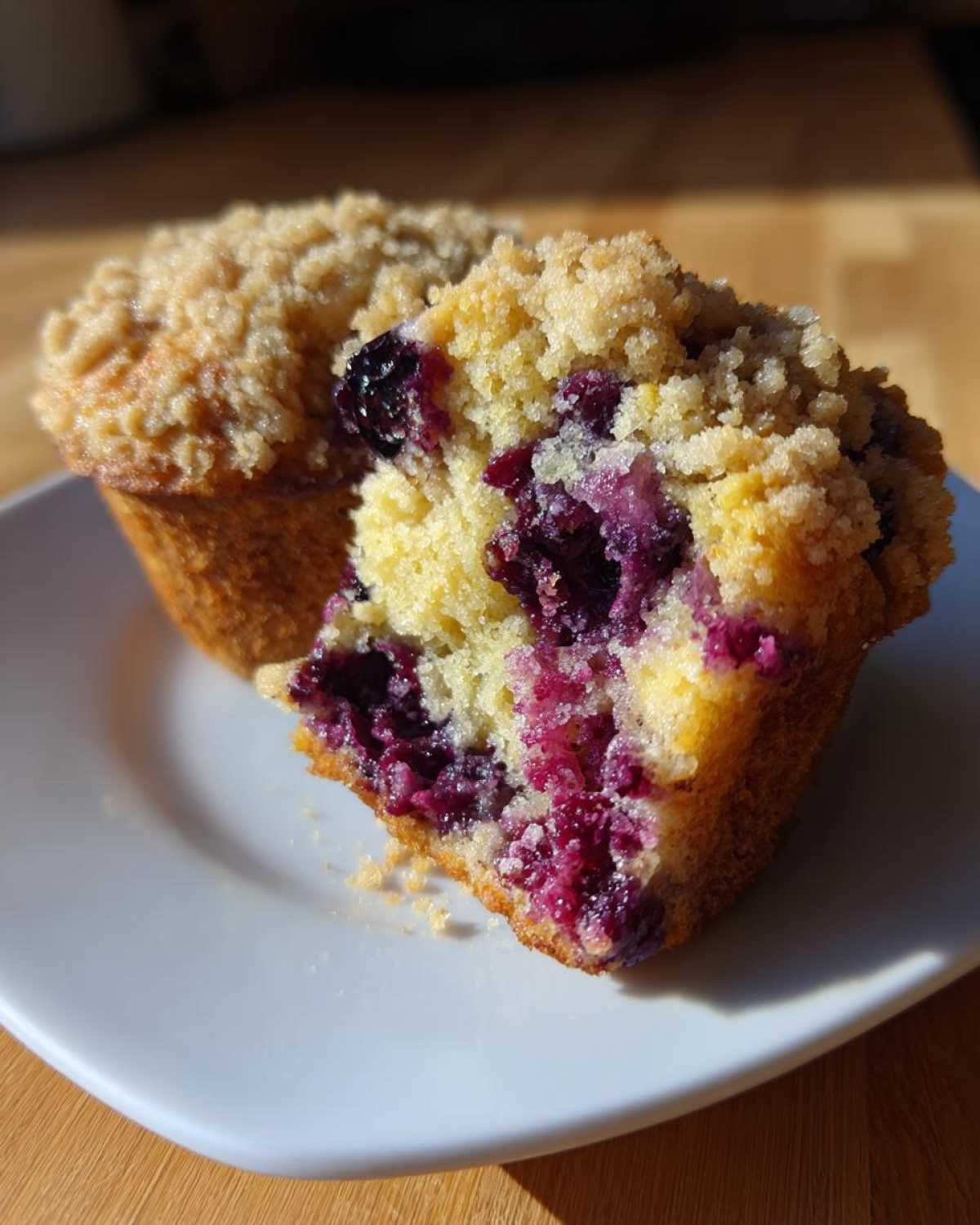 Close-up of a fluffy blueberry muffin cut in half, showing juicy berries and a crumbly streusel topping.