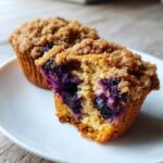 Close-up of a fluffy blueberry muffin cut in half, showing moist interior and rich blueberry filling, topped with streusel.