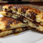 Close-up of fluffy chocolate chip pancakes cut in half, showing melted chocolate chips inside.