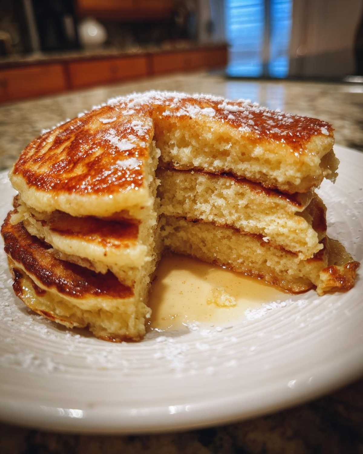 A stack of fluffy coconut flour pancakes cut to show the interior texture, drizzled with syrup and powdered sugar.