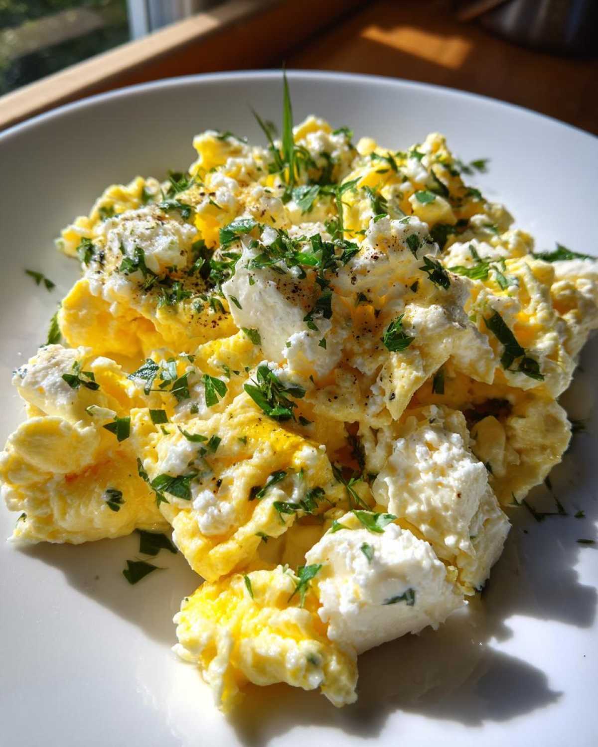 Close-up of fluffy scrambled egg mixed with cottage cheese, topped with fresh parsley and black pepper.